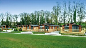 A row of wooden cabins with balconies, set in a grassy area with trees in the background. - Otter Lodge (Skipton)