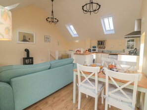 A cozy living room with a teal sofa, a wooden dining table, and white chairs. A kitchen is visible in the background with a stove and a microwave. - Wood Cottage (Middlesbrough)