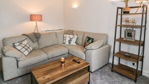 A modern living room with a grey sectional sofa, a wooden coffee table, and a metal shelving unit with decorative items. - Ivy Bank (Thornhill)