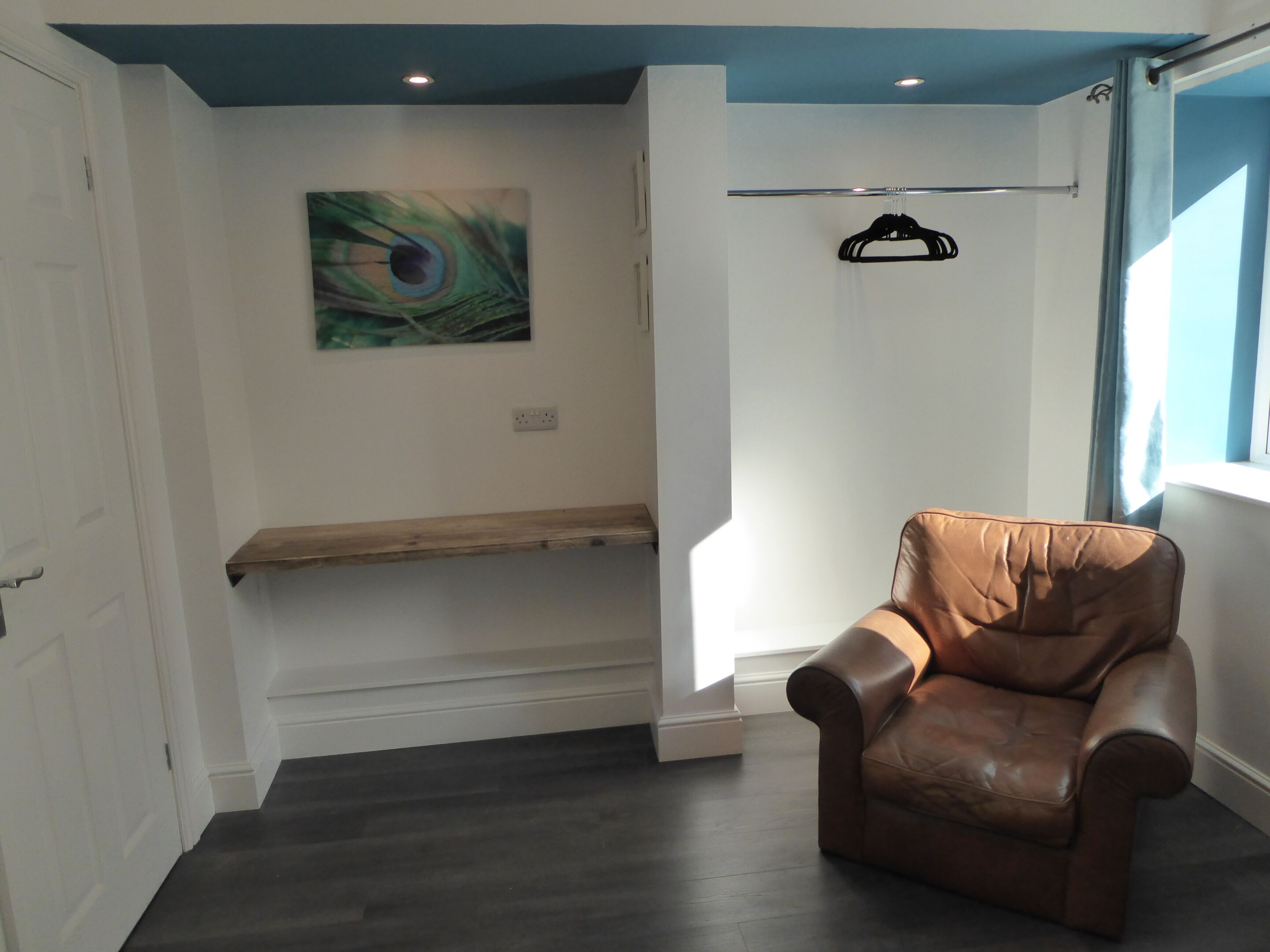 A room with a brown leather chair, a bench, a peacock feather artwork, and a window.