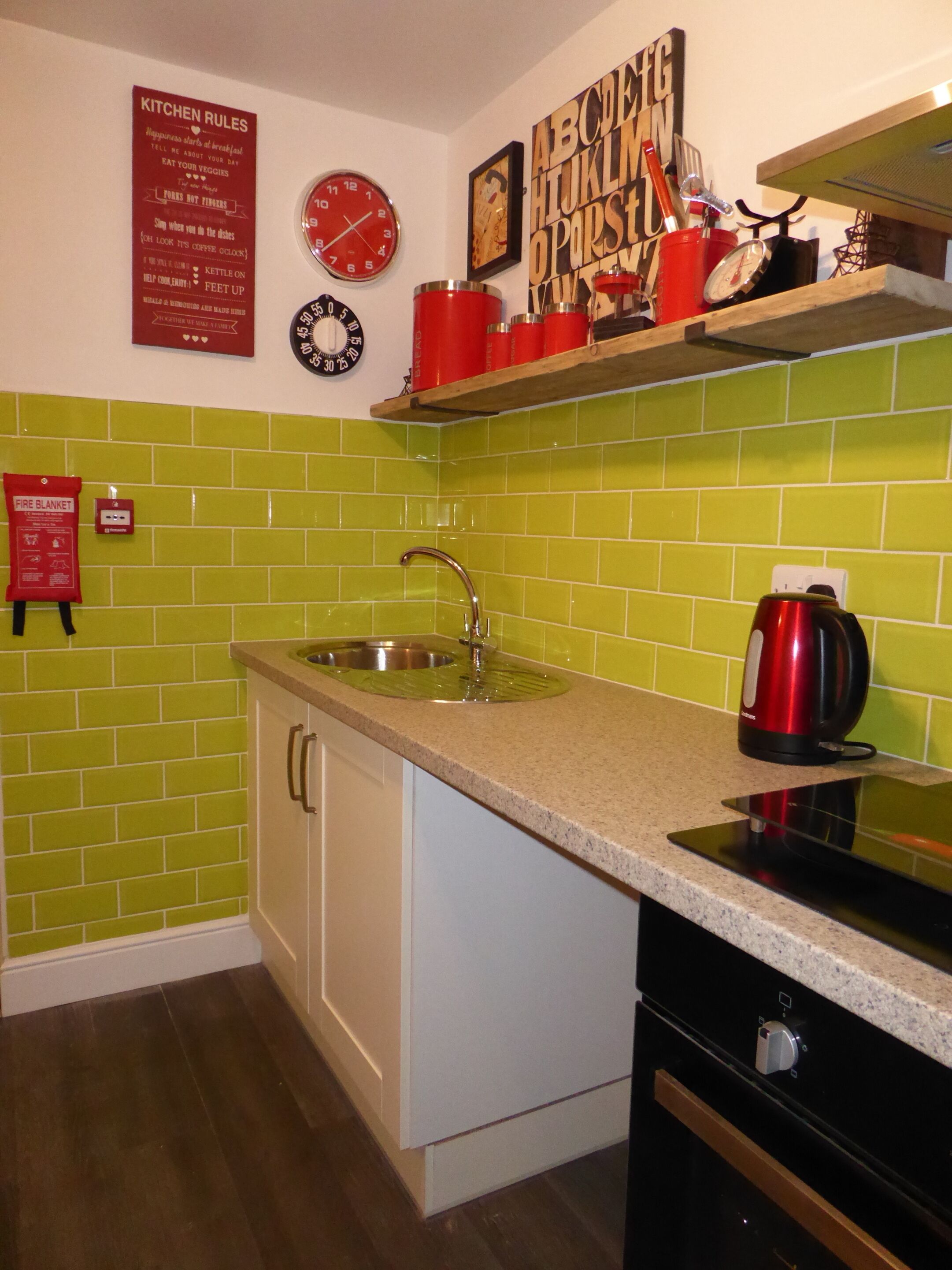 A kitchen with green tiles, a sink, a stove, and a clock.
