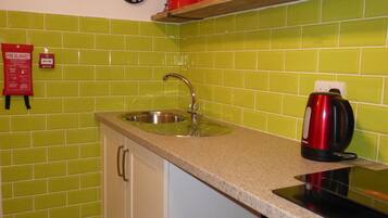 A kitchen with green tiles, a sink, a stove, and a clock.