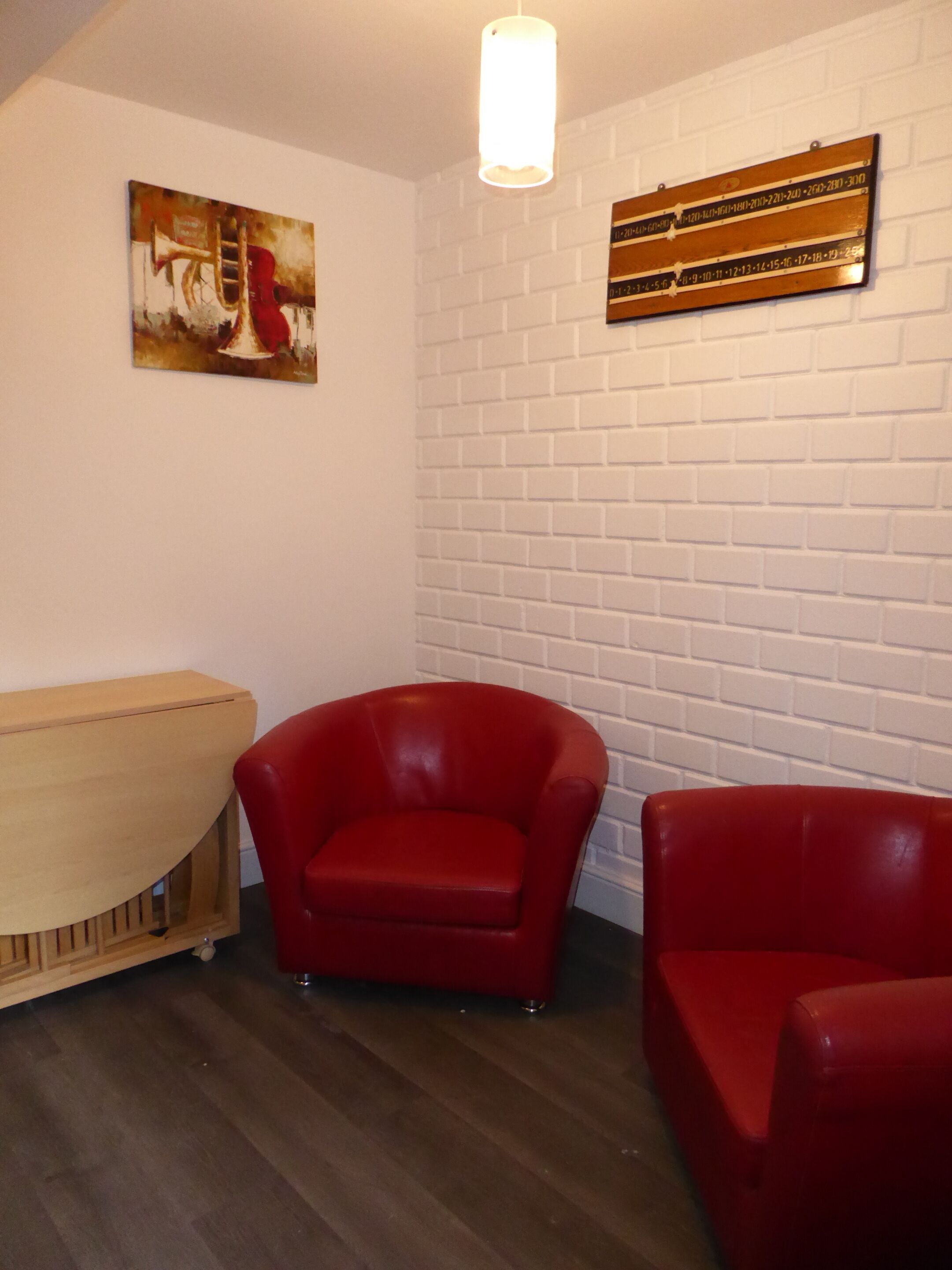 Una habitación con pared de ladrillo blanco, un armario de madera y dos sillas rojas.
