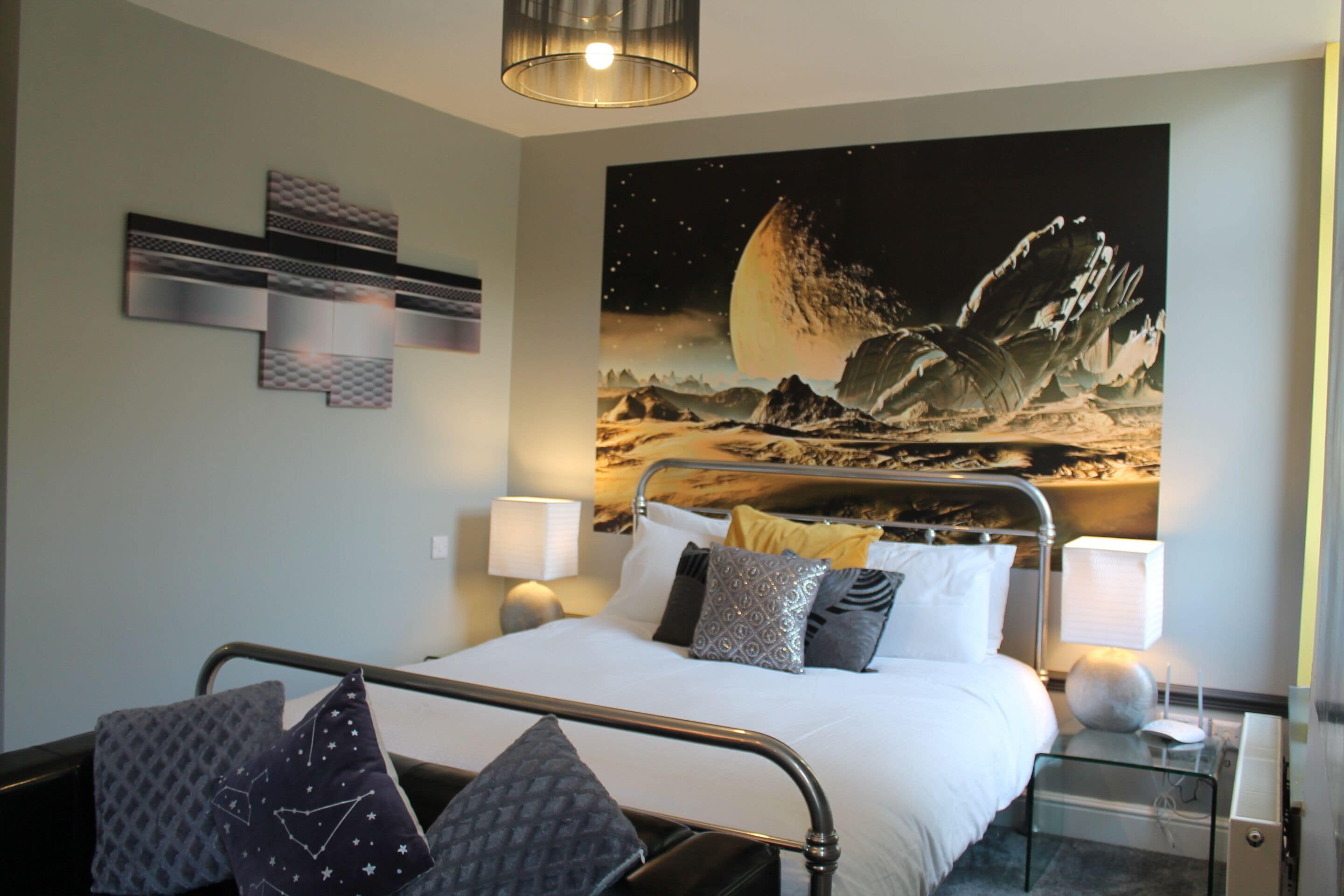 Ett hotellrum med en säng, sängbord, en lampa och en stor väggmålning som föreställer en himmelsk scen.