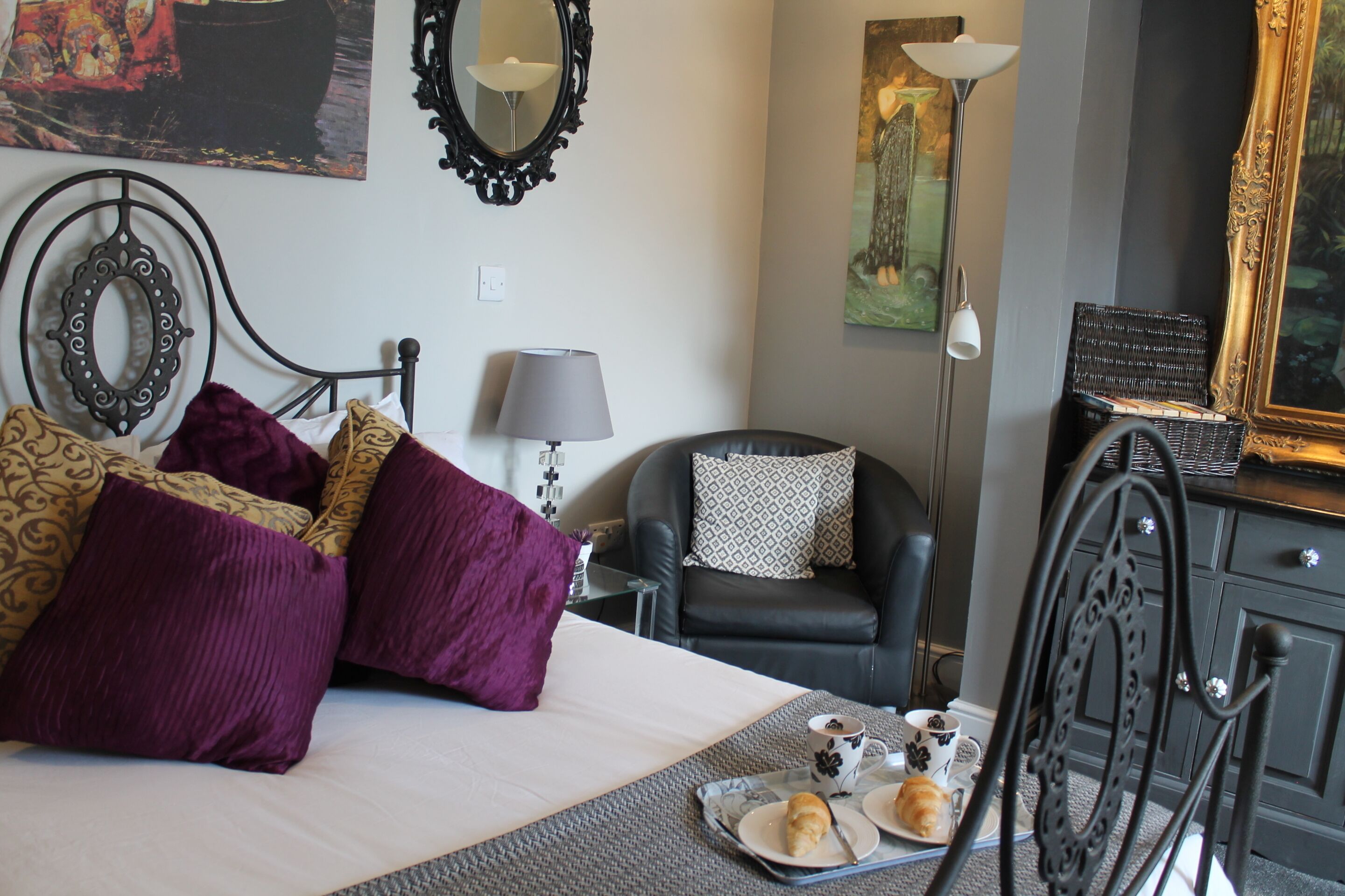 A neatly arranged hotel room with a bed, a chair, a desk, and a tray with pastries.