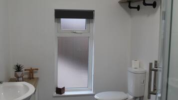 Une salle de bain comprenant des toilettes, une fenêtre, un lavabo et un espace douche.