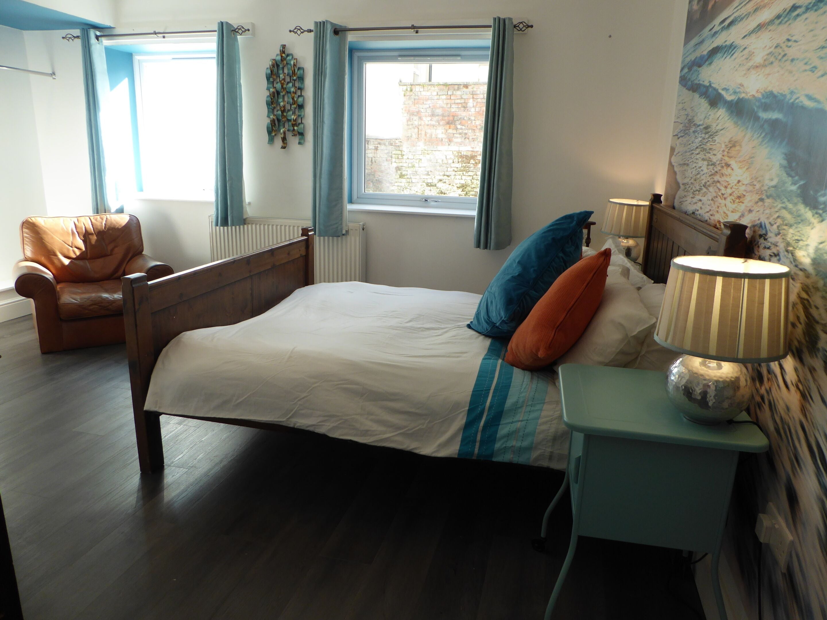 A bedroom with a bed, a chair, a lamp, and a view of the outside.