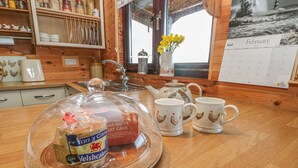 Une table en bois sur laquelle se trouve un gâteau sous un cloche de verre, deux tasses ornées de motifs de poulets, une théière et un calendrier du mois de février 2020.