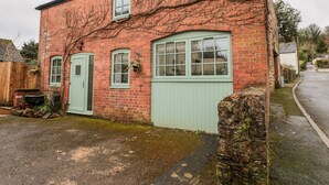 A red brick building with a green door and windows, a sign reading "OSTLERS" above the door, and a stone wall in front.