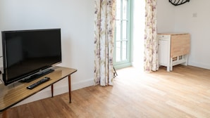 A modern living room with a flat-screen TV on a wooden stand, a remote control, a small wooden side table, and a white cabinet.