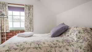 A bedroom with a bed, floral bedding, a window with curtains, and a brick wall.