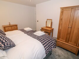 A bedroom with two beds, a wooden wardrobe, a bedside table with a mirror, and a small cabinet.