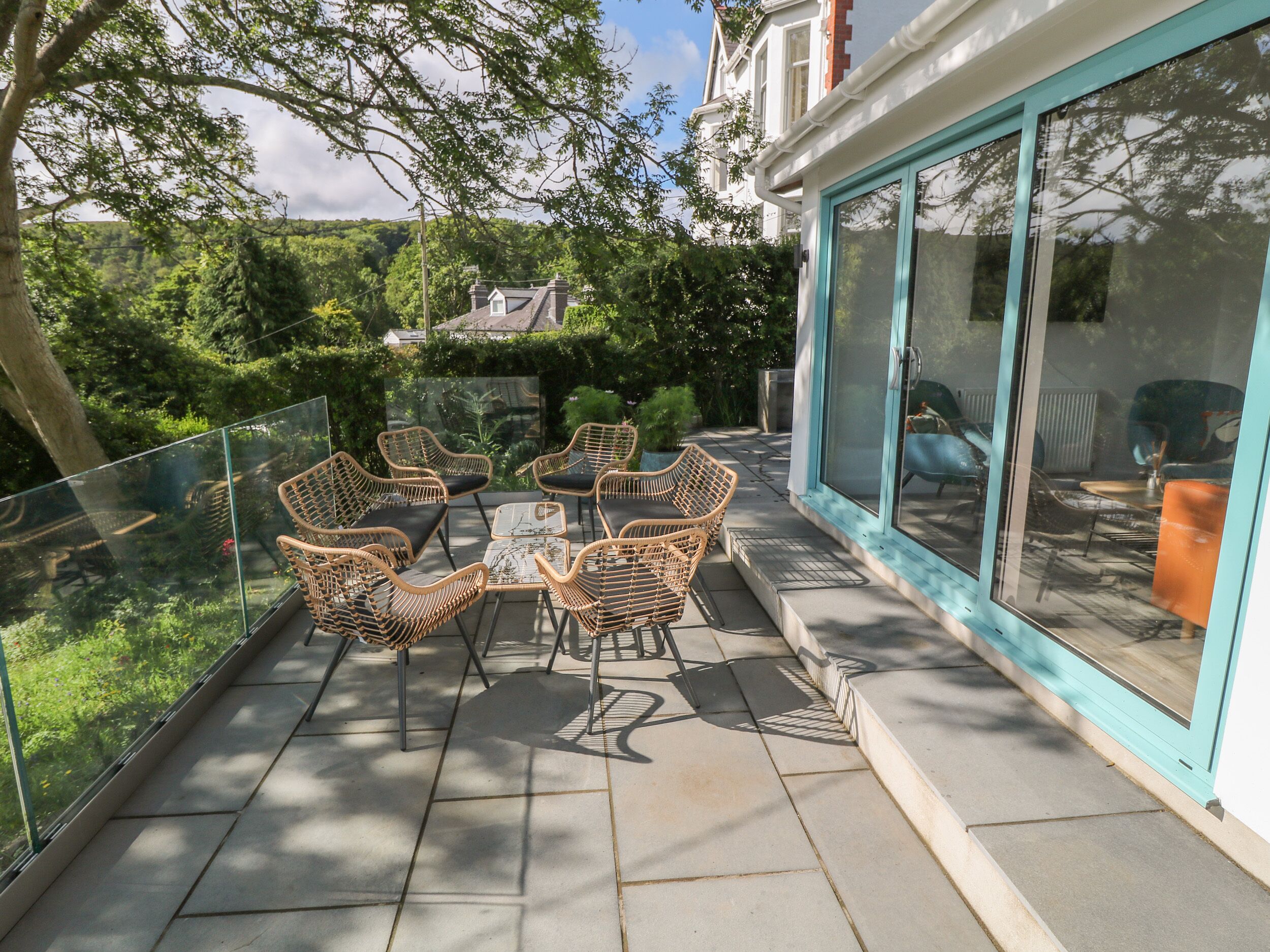Une terrasse extérieure dotée de meubles en osier et d’une balustrade en verre.