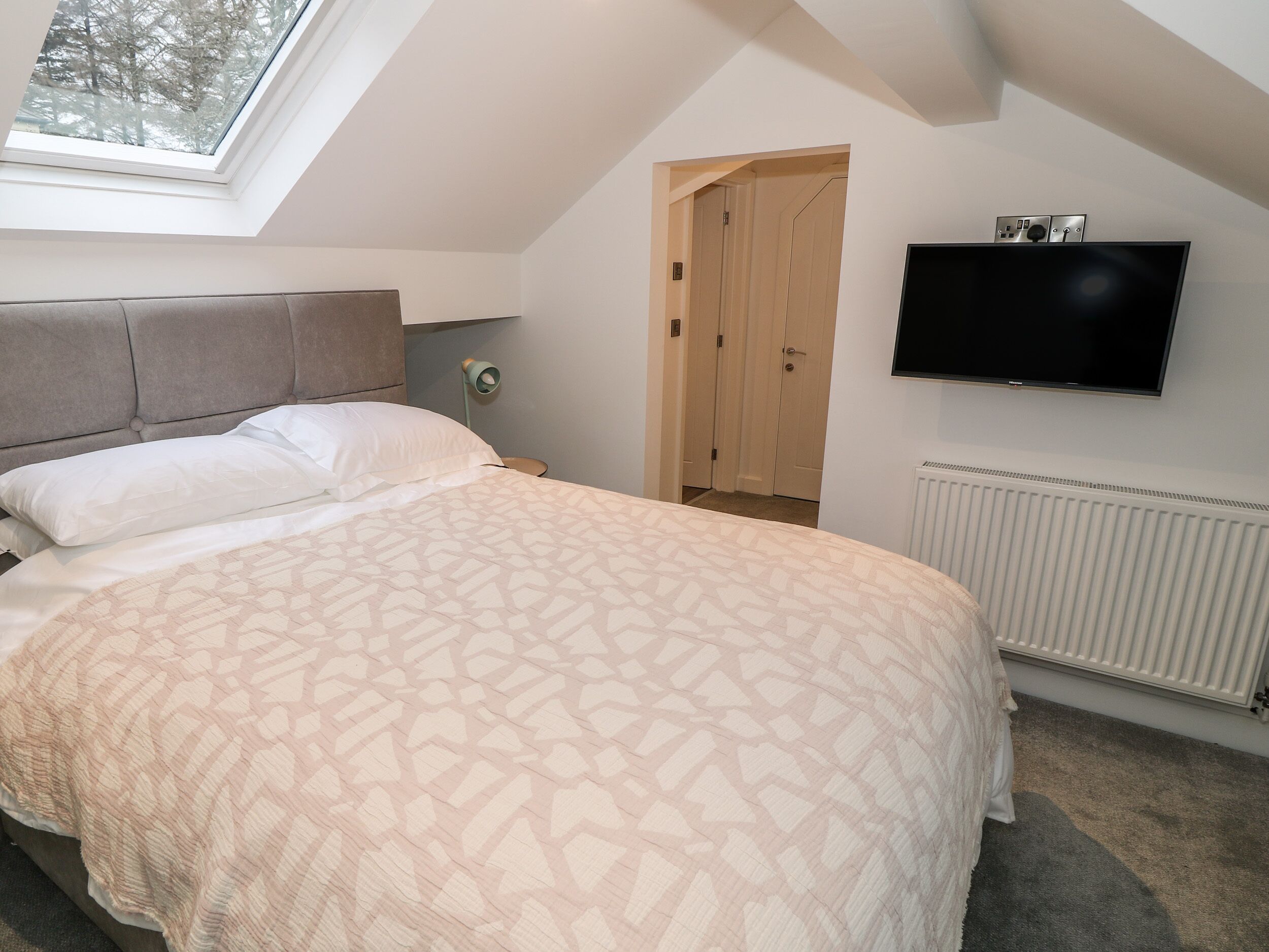 A bedroom with a bed, a TV, a window, and a door.