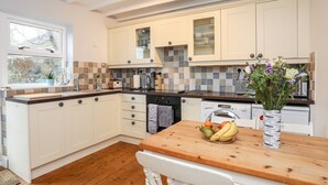 A modern kitchen with white cabinets, a wooden countertop, and a window with a view of greenery. - The Granary - Rhoscolyn (Holyhead)