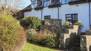 A white building with multiple windows and a stone wall with potted plants. - The Granary - Rhoscolyn (Holyhead)