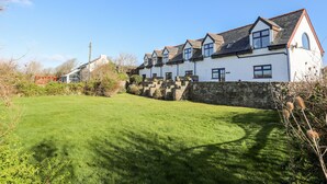 A row of white houses with dark roofs and stone walls, set in a green landscape with a clear sky. - The Granary - Rhoscolyn (Holyhead)