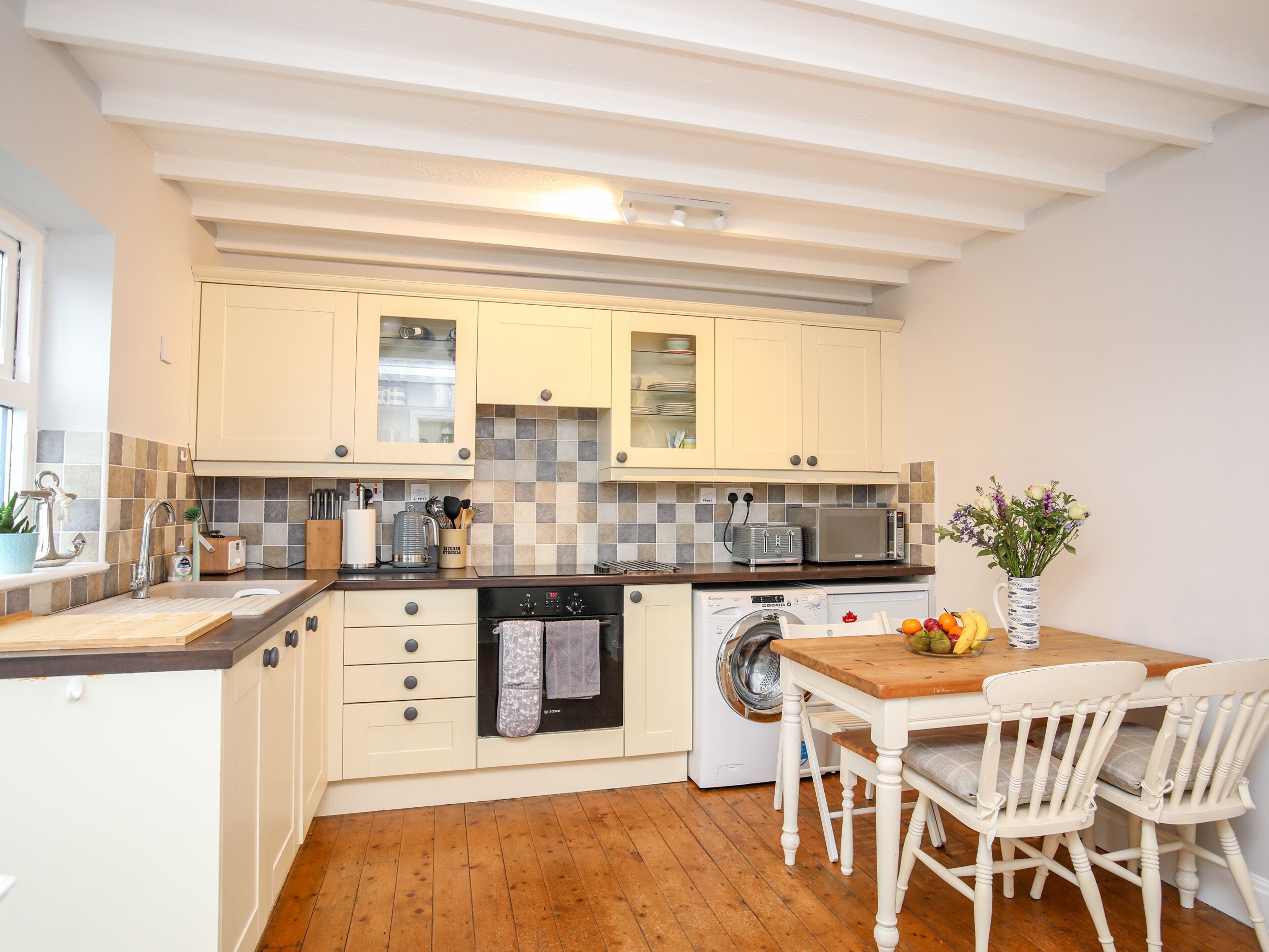 Cocina compacta con armarios blancos, microondas, lavadora y comedor con dos sillas y una mesa.
