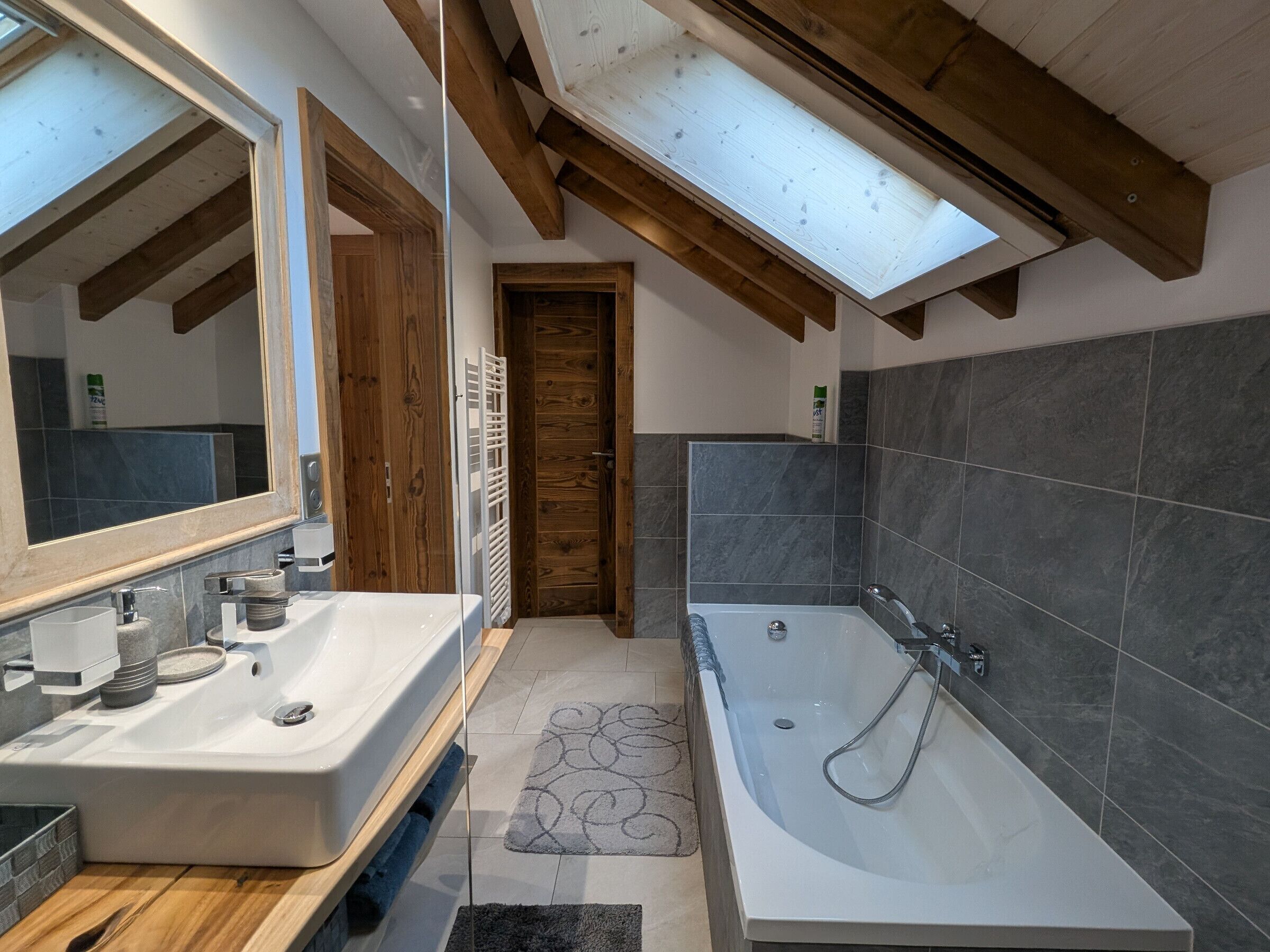 Un baño moderno con tragaluz, un espejo grande, una bañera y techo de madera.