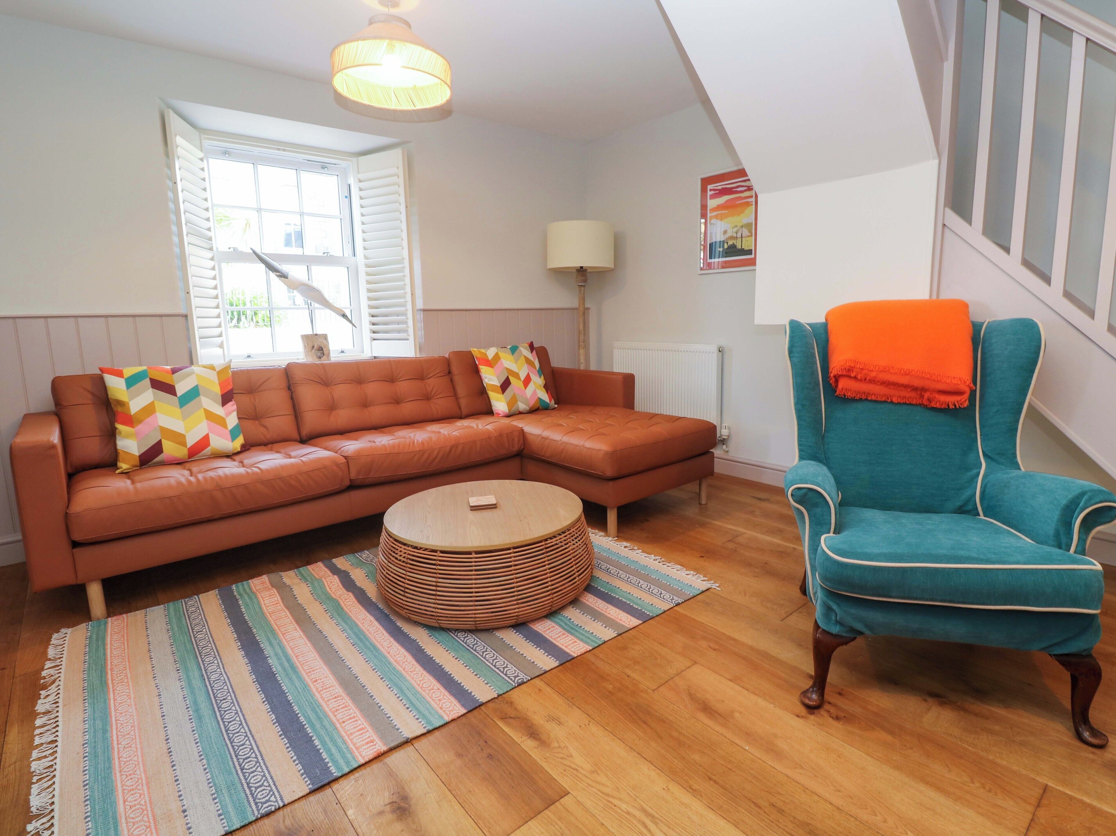 A living room with a brown leather sofa, a teal armchair, a round coffee table, and a patterned rug.