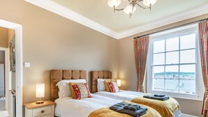 A double bed with two pillows, a bedside table with a lamp, and a window with curtains.