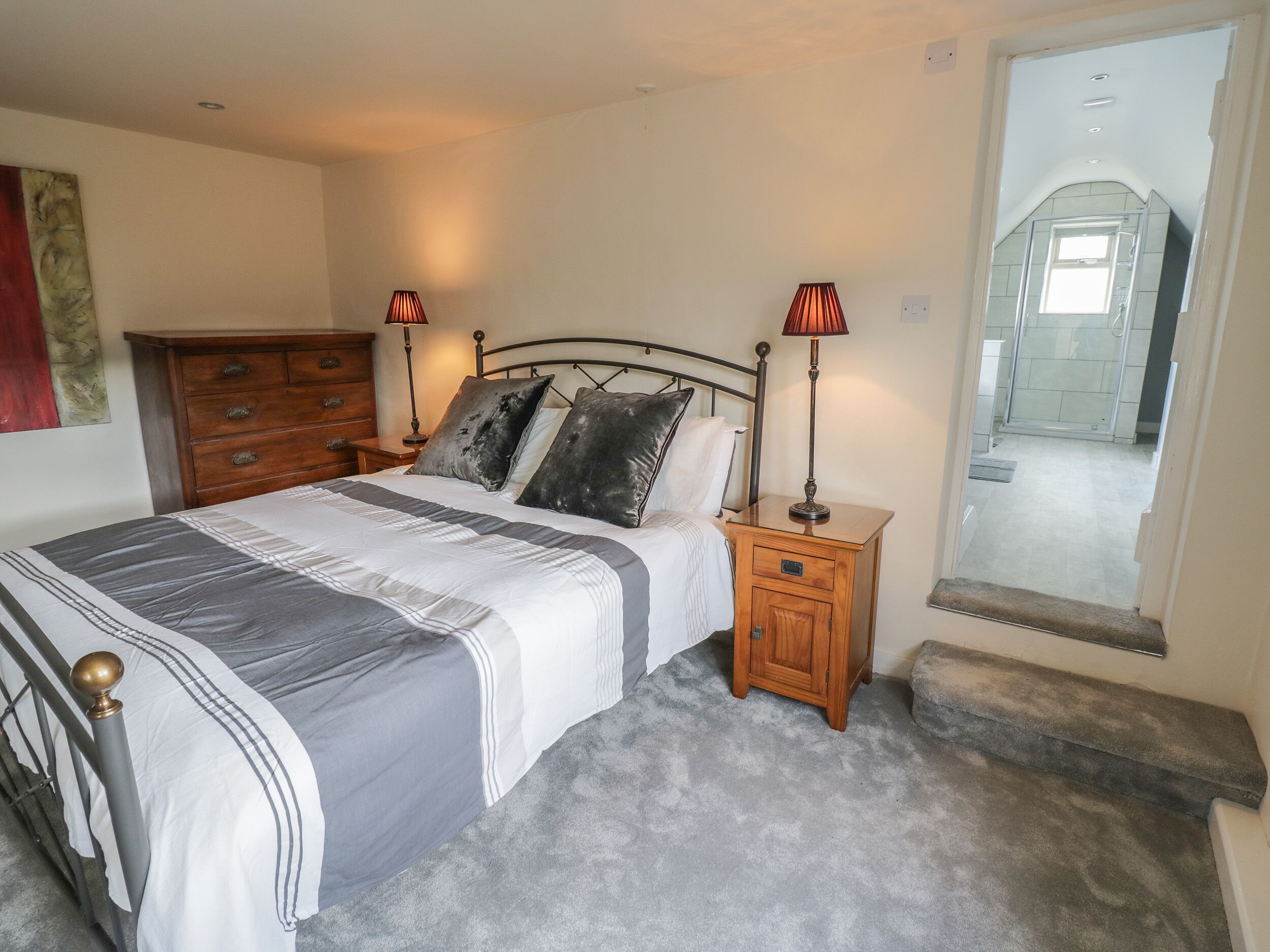 A bedroom with a bed, two bedside tables with lamps, a wooden dresser, and a large mirror.