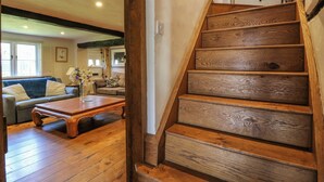 A wooden staircase leading to an upper floor, a living room with a sofa, a coffee table, and a vase of flowers. - Bakehouse Farm (Princes Risborough)