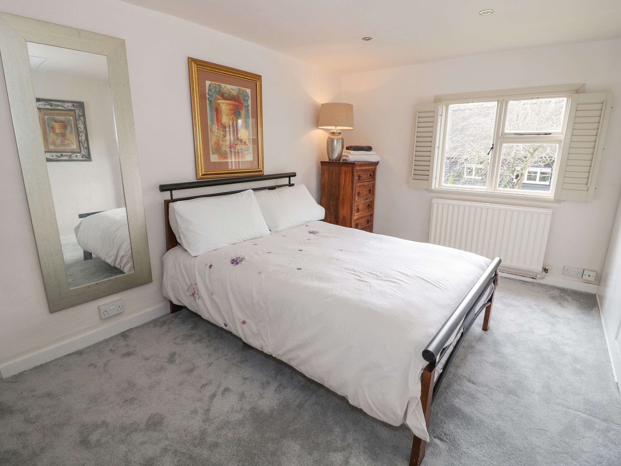 A bedroom with a bed, a dresser, a mirror, a window, and a radiator.