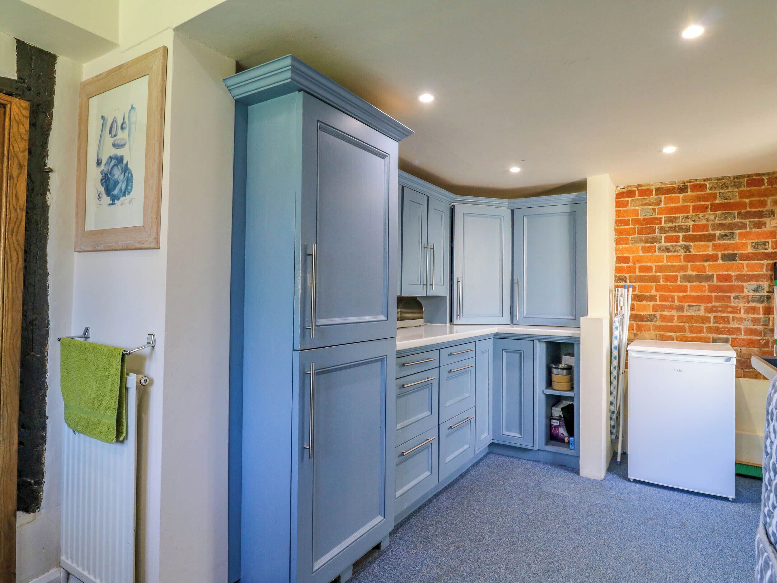A kitchen with blue cabinets, a white refrigerator, and a brick wall.