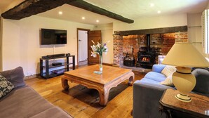 A cozy living room with a wooden coffee table, a sofa, a television, and a fireplace. - Bakehouse Farm (Princes Risborough)