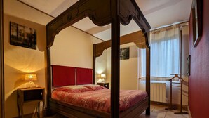 Ein Bett mit Baldachin, ein rotes Kopfteil, ein weißer Teppich und ein Nachttisch aus Holz mit einer Lampe.