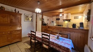 Ein Holztisch mit Stühlen, eine Küchenzeile mit Geräten und eine Holzbalkendecke.