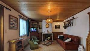 Ein gemütliches Wohnzimmer mit Kamin, einem grünen Sessel, einer braunen Couch und einer Holzzahl.