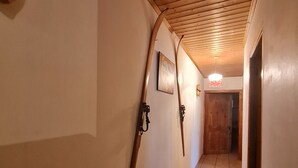 Ein Flur mit Holzbalkendecke, gefliestem Boden und einer Holztür am Ende.