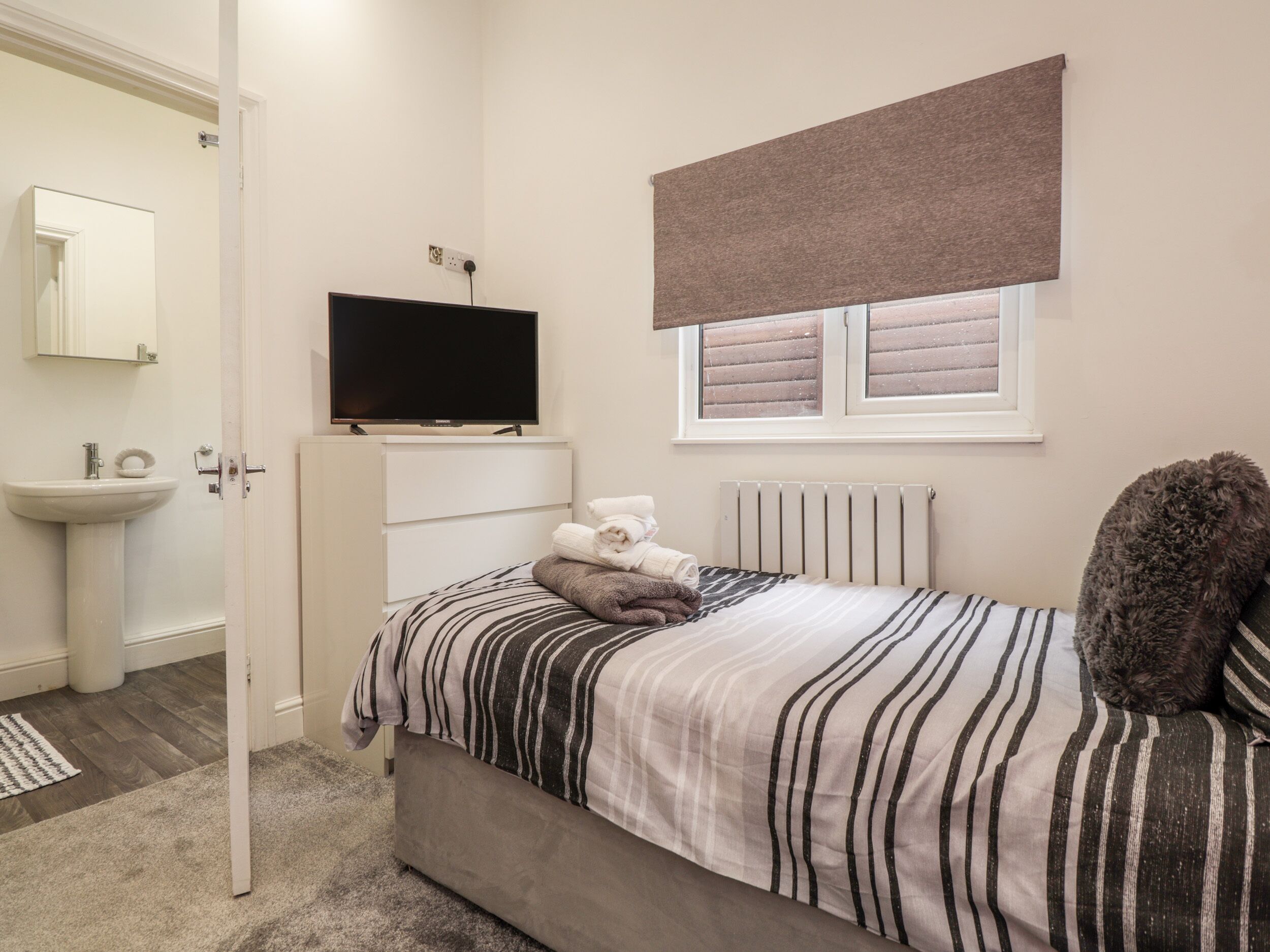 A bedroom with a bed, a television, a radiator, and a window with blinds.