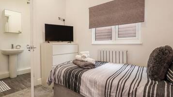 A bedroom with a bed, a television, a radiator, and a window with blinds.