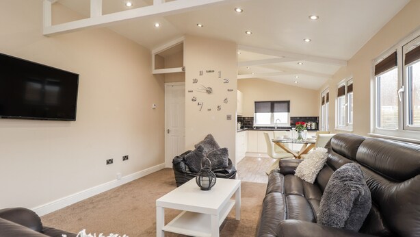 A modern living room with a sofa, a coffee table, and a TV mounted on the wall. - Sparrows Den Lodge (Winchelsea)