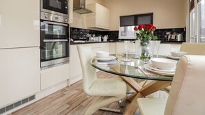 A modern kitchen with built-in appliances, a dining area with a glass table, and a vase with red flowers. - Sparrows Den Lodge (Winchelsea)