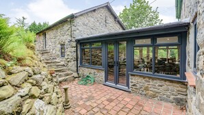 A stone building with a brick patio and a glass-enclosed porch. - Groes Heol (Machynlleth)