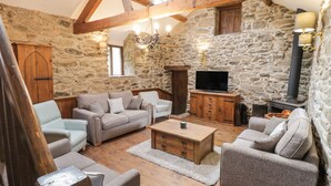 A rustic interior with stone walls, wooden beams, a fireplace, and a television. - Groes Heol (Machynlleth)