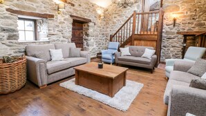 A cozy living room with stone walls, wooden beams, a staircase, and comfortable seating. - Groes Heol (Machynlleth)