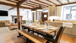 A dining area with a wooden table set for four, surrounded by chairs, in a room with exposed wooden beams and a stone fireplace. - Groes Heol (Machynlleth)