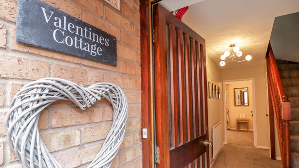 Pared de tijolos com uma placa indicando "Valentines Cottage" e uma decoração em formato de coração.