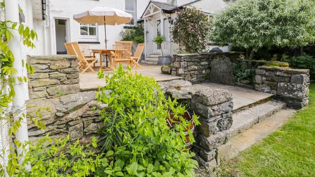 Un edificio blanco con una escalera de piedra que lleva a un patio con muebles y una mesa de madera.