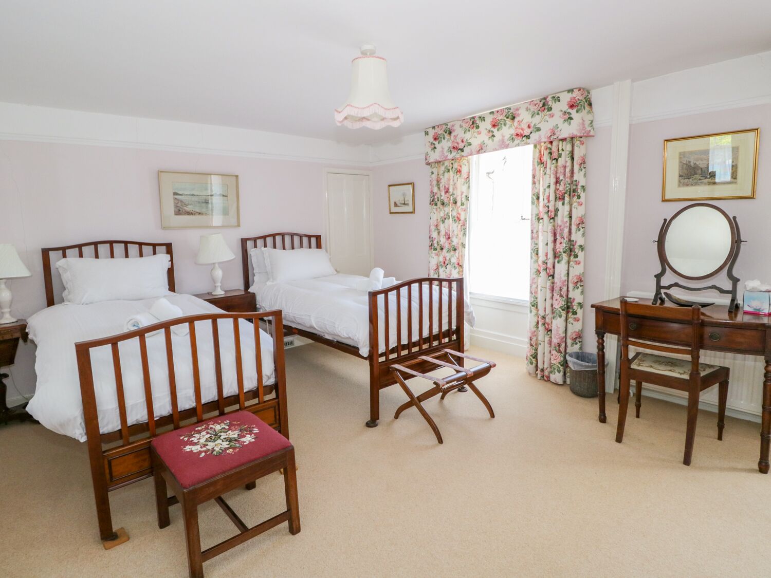 A bedroom with two wooden beds, a wooden chair, a desk with a mirror, and a window with floral curtains.