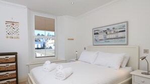 A neatly arranged bedroom with a large bed, a bedside table with a lamp, a dresser, and a view of the street through a window. - 2 Embankment House (Dartmouth)