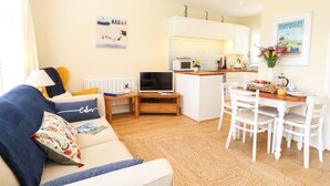 Un salon confortable avec un canapé, une télévision et un petit coin cuisine comprenant une table et des chaises.