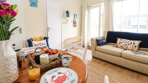 Un salon chaleureux avec une table à manger dressée pour le petit-déjeuner, un canapé et une vue sur l’extérieur grâce à de grandes fenêtres.
