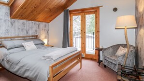 Un dormitorio acogedor con techo de madera, una cama con ropa de cama gris, una silla y una lámpara.