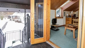 Interior de madera con televisor, un tablero de ajedrez y ventana con vistas a un paisaje nevado.